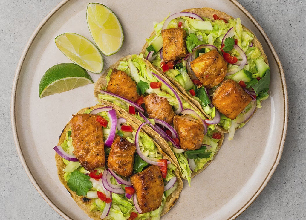 Lachs-Tacos auf einem Teller mit Limetten-Spalten und die Bewegung zeigt wie Soße darauf gegeben wird
