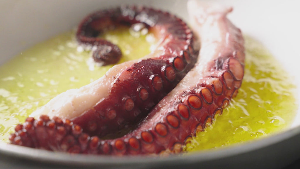 Oktopusarme in einer Pfanne sprudelnd in Olivenöl